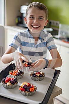 Portrait of happy baby boy posing with baking sheet full of summer dessert ready to cooking at home