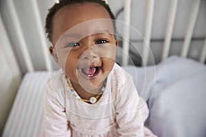 Portrait Of Happy Baby Girl Playing In Nursery Cot