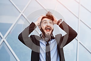 Portrait of happy bearded businessman with headphones on neck, skycraper windows background.