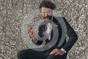 Happy bearded elegant man in black tuxedo holding hand up and gesticulating photo