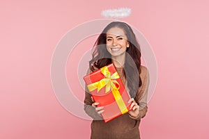 Portrait of happy beautiful angelic young woman with halo holding big present and smiling to camera, satisfied with gift