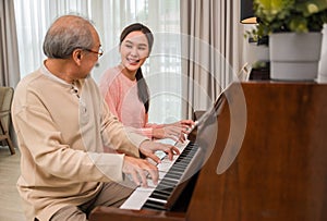 Portrait of happy beautiful Asian woman and her father sitting playing piano and singing together having fun and enjoying in