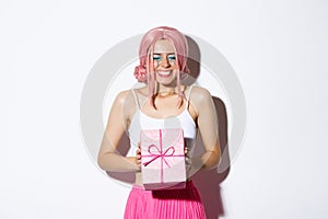 Portrait of happy beautiful b-day girl looking excited, receiving birthday gift and smiling joyfully, standing in pink