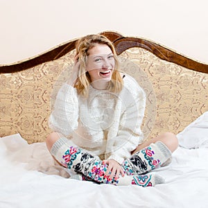 Portrait of happy beautiful blond young woman blue eyes girl in knitted looking at camera and smiling on white bed background