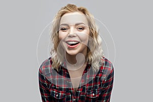 Portrait of happy beautiful blonde young woman in casual red checkered shirt standing, laughing and looking at camera with toothy