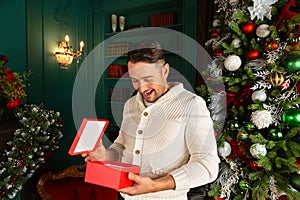 Portrait of happy beautiful emotional man opening Christmas gift box at his home