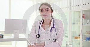 Portrait of happy beautiful female doctor cardiologist in sitting at table in clinic