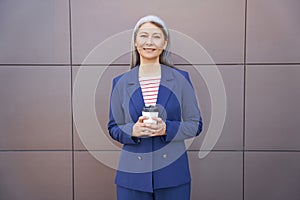 Portrait of a happy beautiful mature business woman wearing eyeglasses and classic suit holding cup of coffee and