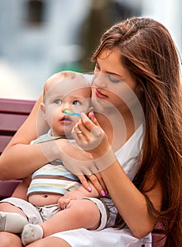 Portrait of happy beautiful mother feed her baby summer outdoors in park.
