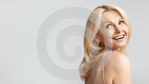 Portrait of happy beautiful senior woman looking back at free space and smiling, posing over light background, panorama