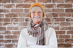 Portrait of happy beautiful senior woman wearing winter cap and scarf - brick wall background