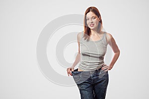 portrait of happy beautiful slim waist of young woman in big jeans and gray top showing successful weight loss