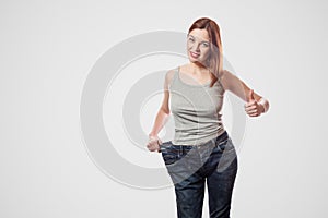 portrait of happy beautiful slim waist of young woman in big jeans and gray top showing successful weight loss