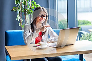 Portrait of happy beautiful stylish brunette young woman in glasses sitting, looking at her laptop screen on video call, pointing