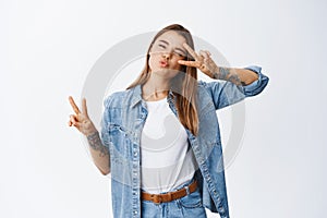 Portrait of happy beautiful woman in casual clothes, showing v-signs and pucker lips kissing, having fun, standing