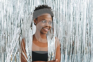 Portrait of happy beautiful young African American woman in black top on the sparkly silver background, party time