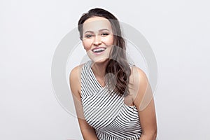 Portrait of happy beautiful young brunette woman with makeup and striped dress standing and looking at camera with toothy smile