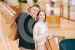 Portrait of happy beautiful young couple holding shopping paper bags with purchases and looking at camera.