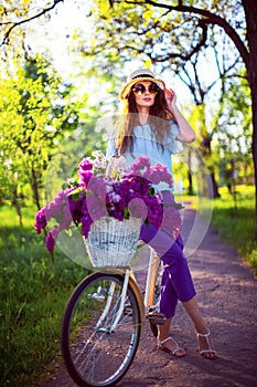 Beautiful young girl with vintage bicycle and flowers on city background in the sunlight outdoor.