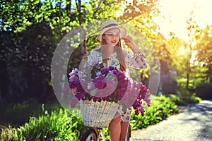 Portrait of a happy beautiful young girl with vintage bicycle and flowers on city background in the sunlight outdoor