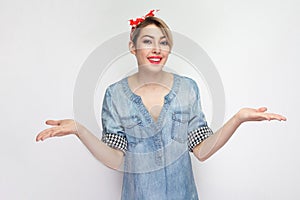 Portrait of happy beautiful young woman in casual blue denim shirt with makeup and red headband standing raised arms and looking