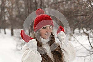 Portrait of happy beautiful young woman in knitted red hat and mittens and woolen sweater in winter park.Ladies knitwear