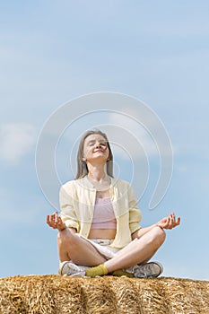 Portrait of happy beautiful young woman meditating sitting in the hay against blue sky. Unity with nature