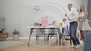 Portrait of happy big caucasian family holding clothes of each other and moving around table. Cheerful people partying