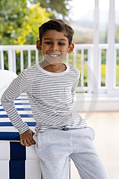 Portrait of happy biracial boy wearing pyjamas in bedroom in front of window with view of treetops