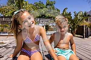 Portrait of happy biracial brother and sister sitting by the swimming pool