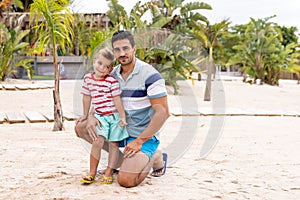 Portrait of happy biracial father and son embracing and smiling at beach, with slow motion