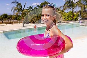 Portrait of happy biracial girl smiling and holding swim ring by the swimming pool