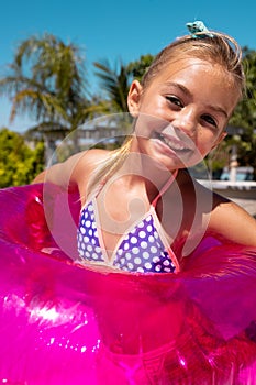 Portrait of happy biracial girl smiling and holding swim ring by the swimming pool