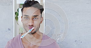 Portrait of happy biracial man brushing teeth in sunny bathroom, copy space, slow motion