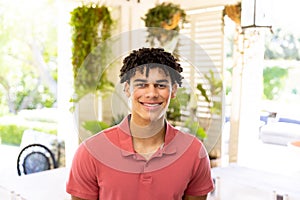 Portrait of happy biracial man with curly black hair smiling at home in sunny room