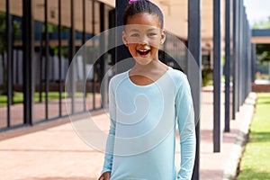 Portrait of happy biracial schoolgirl talking in sunny schoolyard copy space