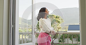 Portrait of happy biracial woman standing at balcony and looking at camera