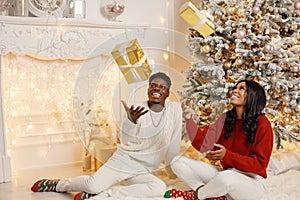 Portrait of happy black couple throwing gifts in the air while sitting near Christmas tree