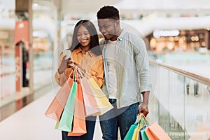 Portrait of happy black couple using phone holding shopping bags