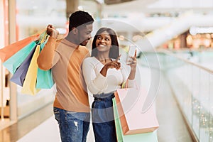 Portrait of happy black couple using phone with shopping bags