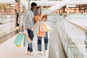 Portrait of happy black couple using phone with shopping bags