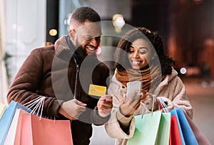 Portrait of happy black couple using smartphone holding credit card