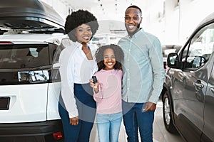 Portrait of happy black family with car key smiling at camera, buying new vehicle in auto dealership
