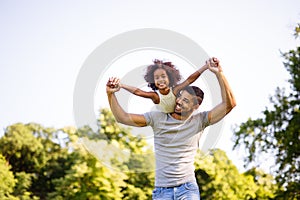 Portrait of happy black father carrying daughter on back outdoors. Family happiness love concept.