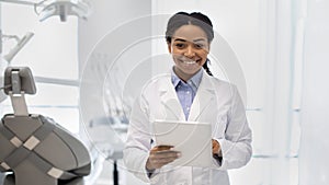 Portrait of happy black female dentist in white coat with digital tablet