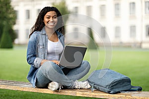 Portrait Of Happy Black Female Student With Laptop Sitting On Bench Outdoors