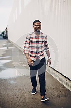 Portrait of a happy black guy in a plaid shirt walking in the city