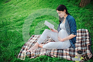 Portrait of a happy black hair and proud pregnant woman in the park. The female model is sitting on grass and The female