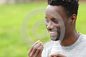 Happy black man taking vitamin pill in the park
