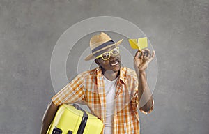 Portrait of happy black tourist holding suitcase and paper plane isolated on gray background